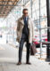 Khaki trench coat over a charcoal windowpane suit with blue tie and brown monk straps, styled on a city sidewalk