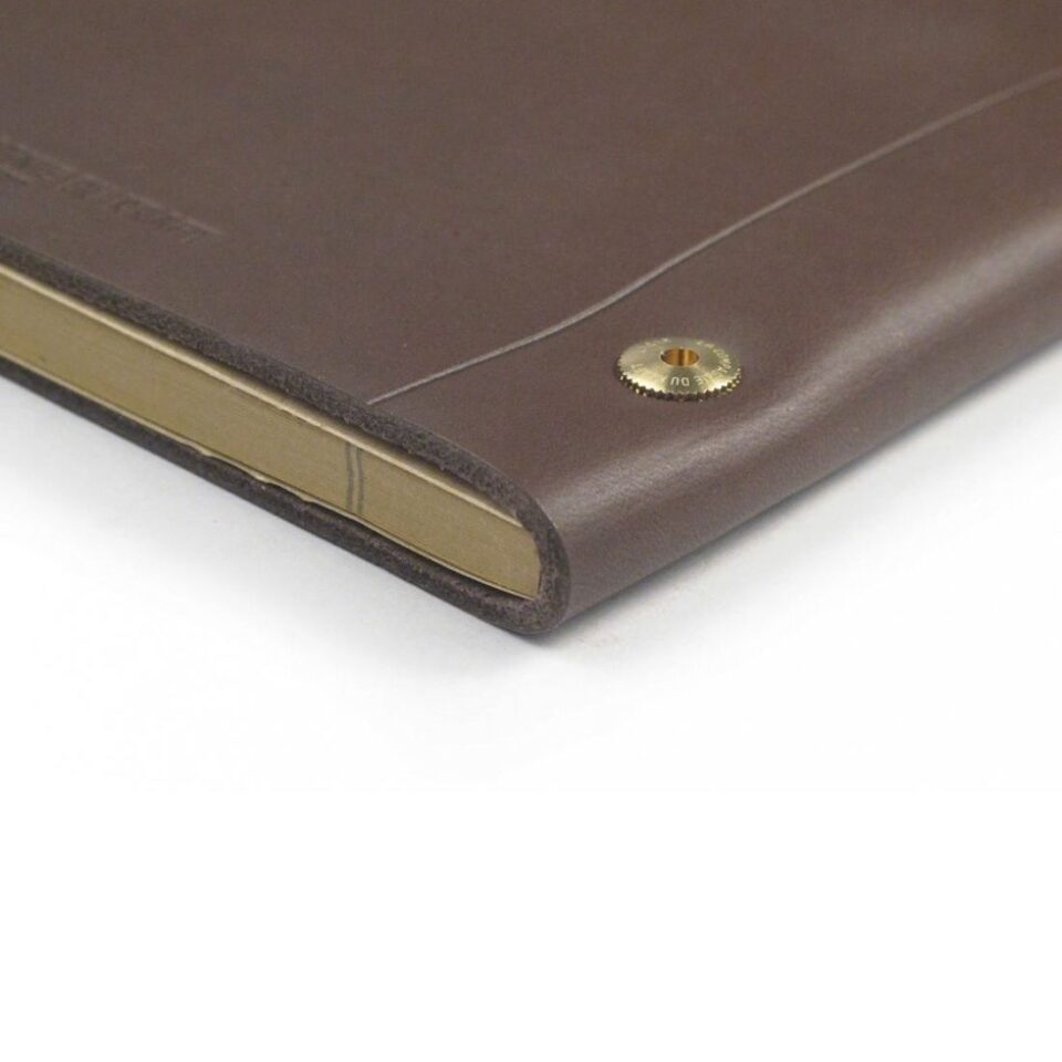 Brown smooth leather notebook cover with brass stud closure, a close-up of the corner and pages