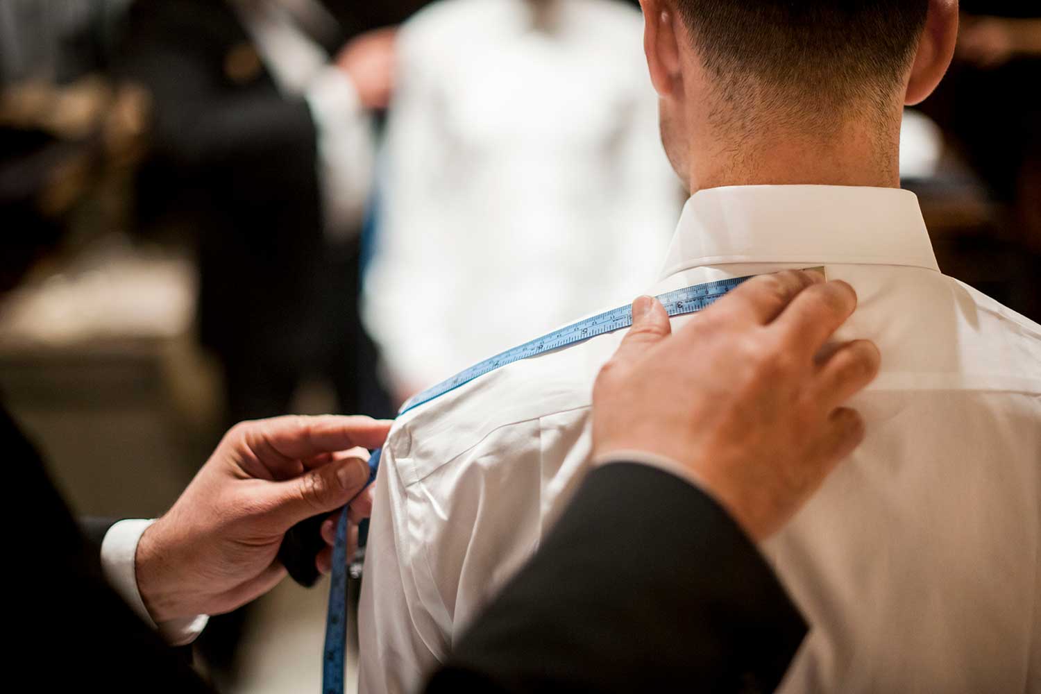 A tailor measures a man's shoulders for a custom or bespoke suit