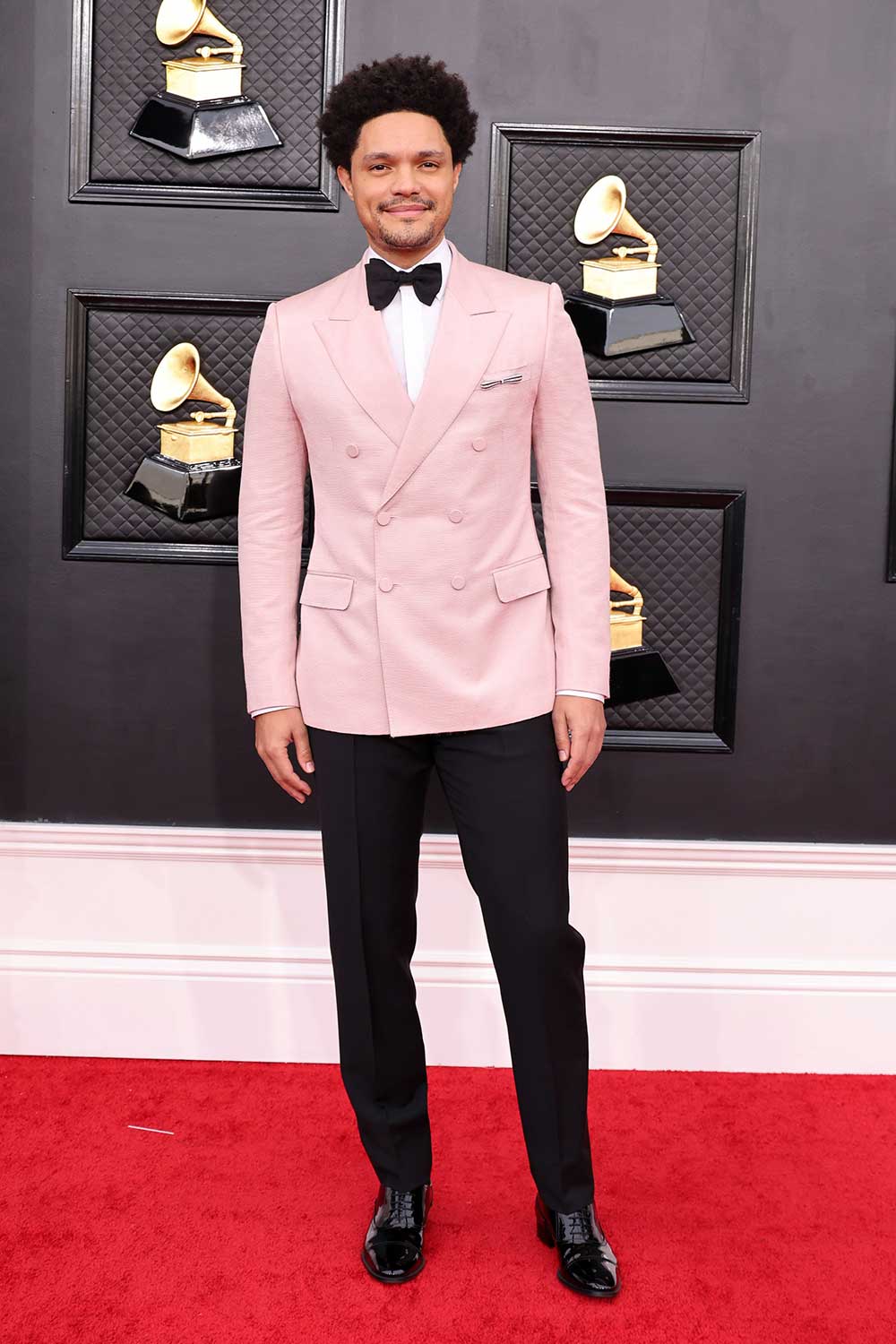Trevor Noah wearing a pink Gucci tuxedo jacket at the 2022 Grammy Awards Red Carpet