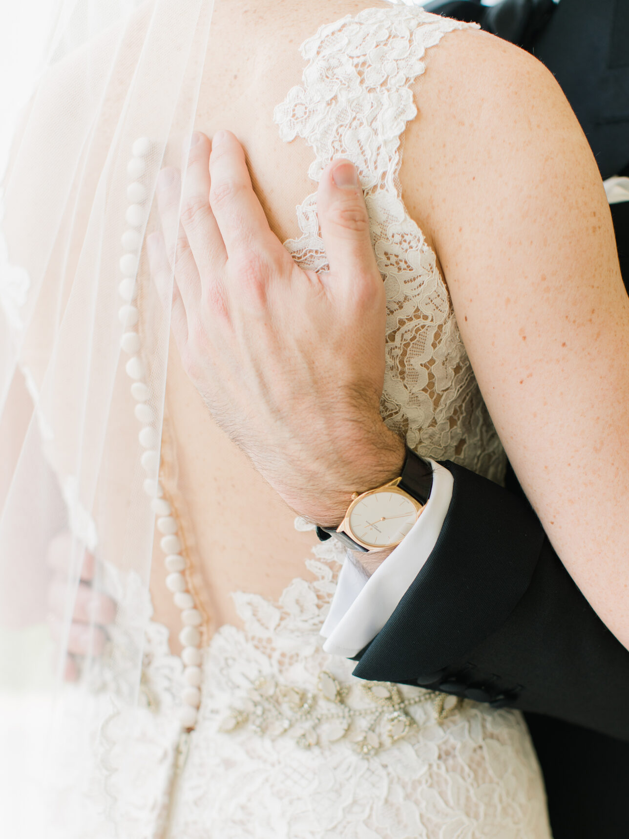 Black tuxedo sleeve with white shirt cuff and gold dress watch on black leather strap, at a wedding