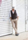 Brown waistcoat with white shirt, tan linen trousers, navy driving loafers and panama hat, worn by a model on a city street