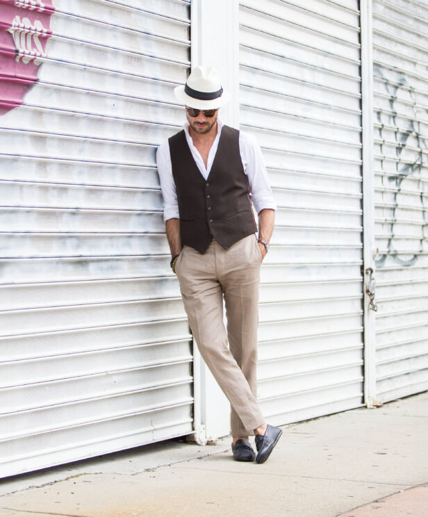 Brown waistcoat with white shirt, tan linen trousers, navy driving loafers and panama hat, worn by a model on a city street