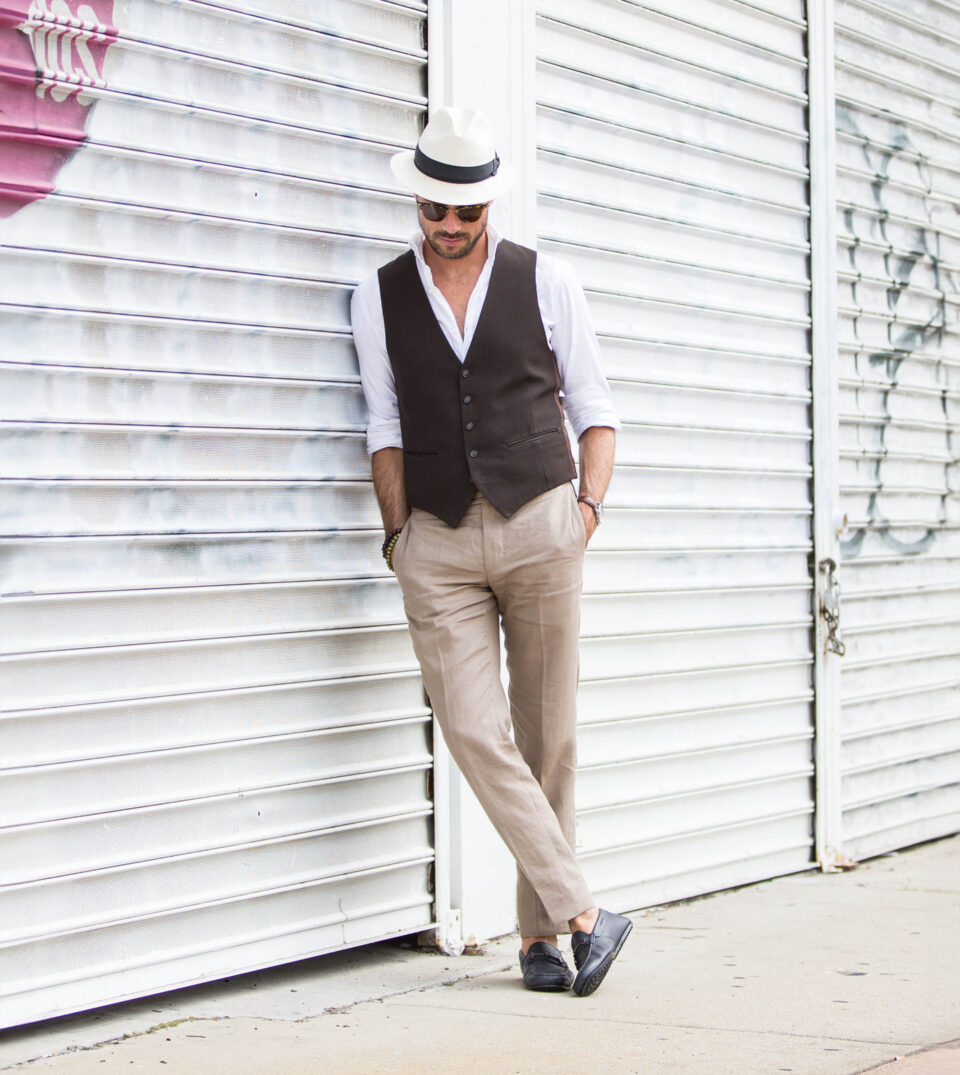 Brown waistcoat with white shirt, tan linen trousers, navy driving loafers and panama hat, worn by a model on a city street