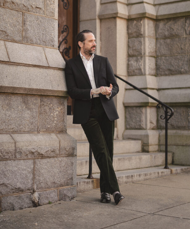 Black flannel sport coat with white shirt, olive corduroy trousers and black loafers, worn by a model outdoors