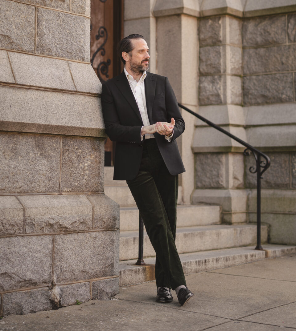 Black flannel sport coat with white shirt, olive corduroy trousers and black loafers, worn by a model outdoors