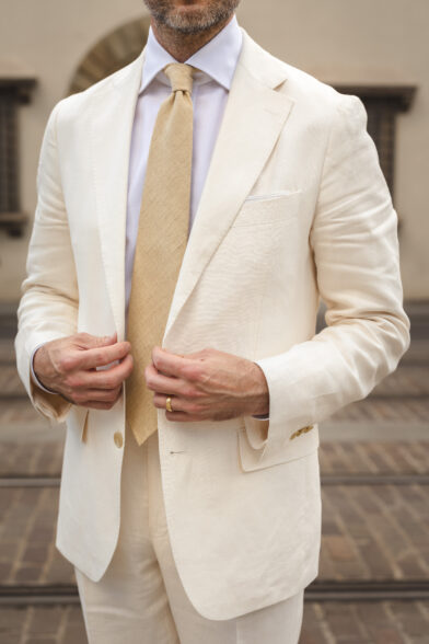 A cream linen suit styled with a white shirt and tan linen tie