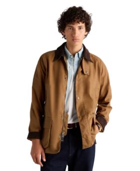 Tan waxed cotton barn jacket with brown corduroy collar, over a light blue shirt and dark jeans, worn by a model