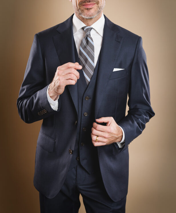 Navy three-piece suit with white shirt, grey striped tie and white pocket square, worn by a model