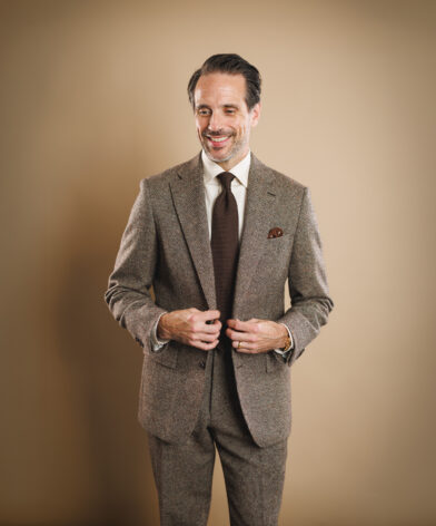 Brown tweed two-button suit with cream shirt, brown knit tie and patterned pocket square, worn by a model