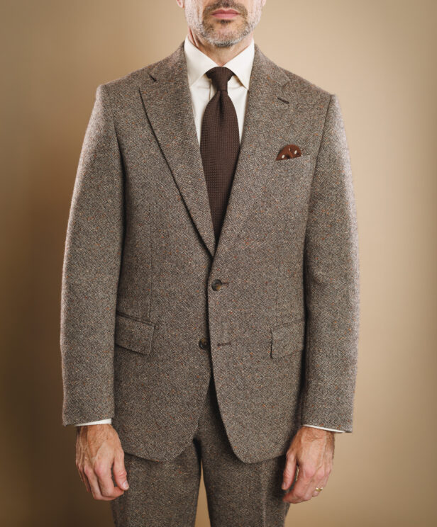 Brown donegal tweed two-button suit with cream shirt, brown knit tie and patterned pocket square, worn by a model