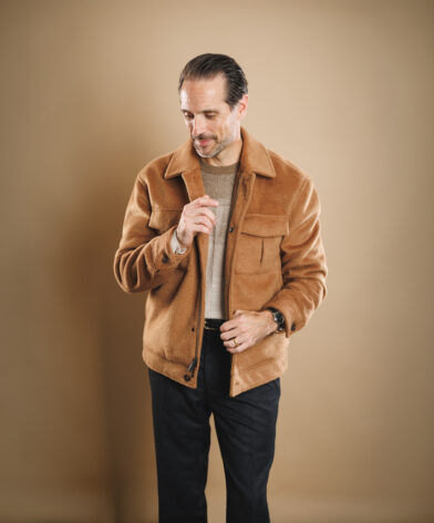 Camel wool zip-front shirt jacket with patch pockets, tan knit sweater and navy trousers, worn by a model