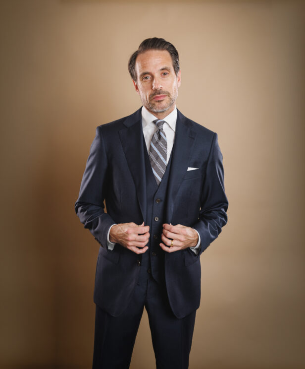 Navy three-piece suit with white shirt, grey striped tie and white pocket square, worn by a model